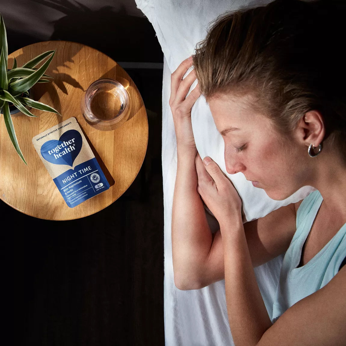 Woman sleeping on a bed with a small table next to her holding a glass of water and a packet labeled 'Together Health'.